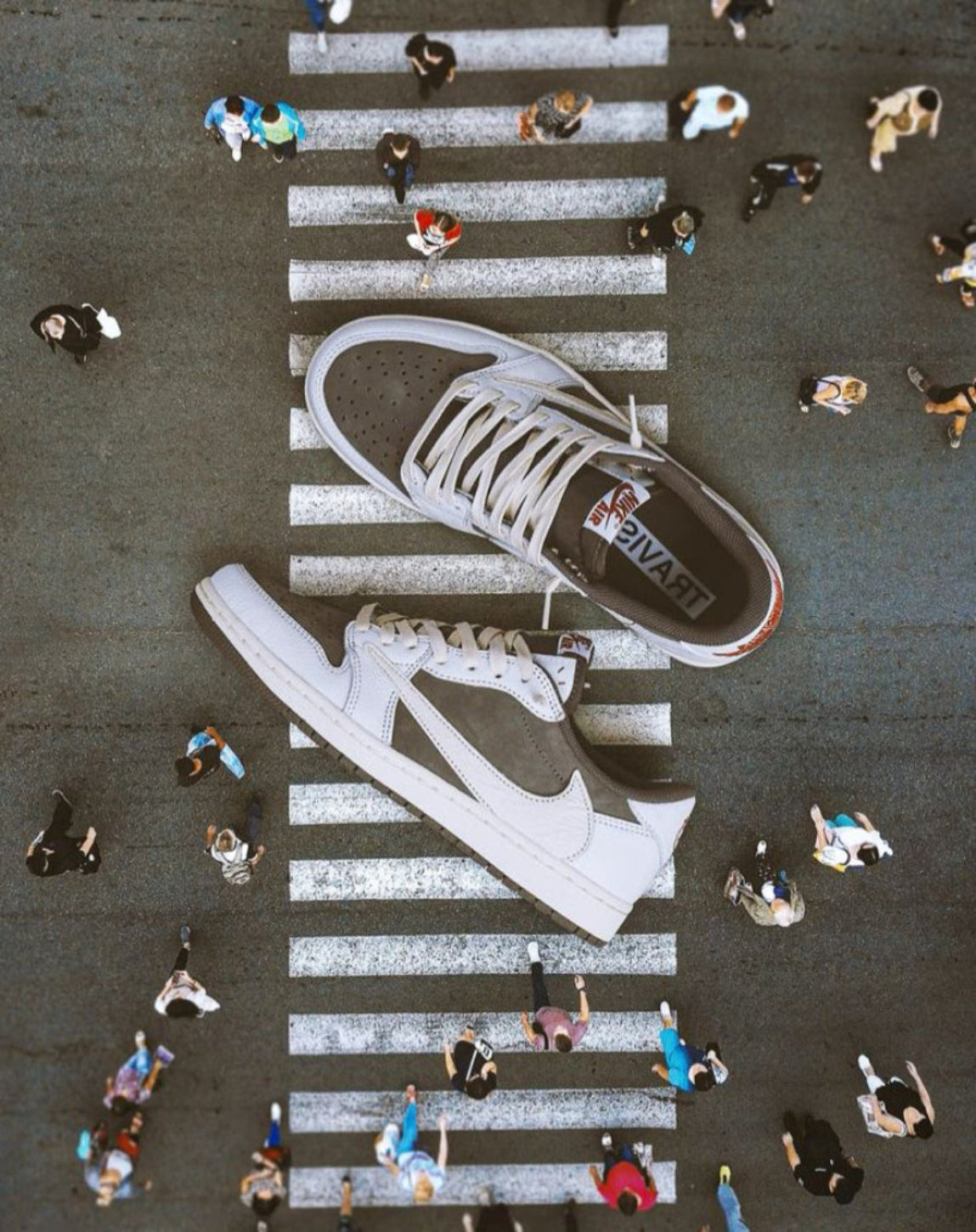 White sneakers with a brand logo on a zebra crossing with people walking around.